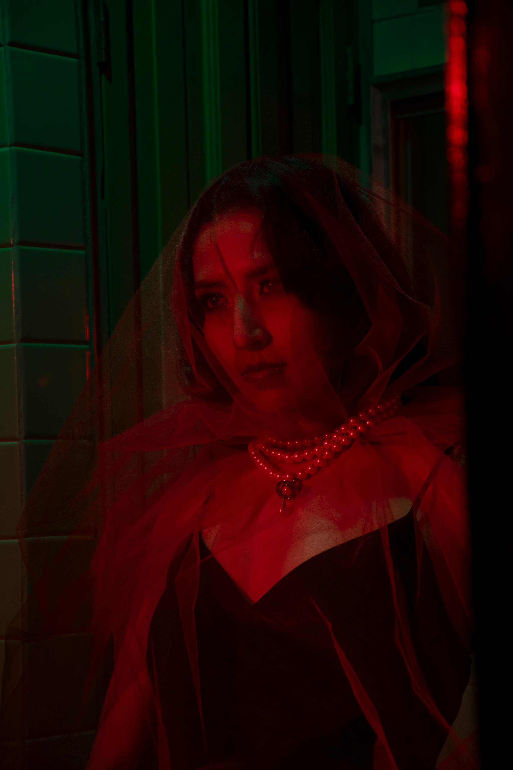 Ücretsiz İnci kolyelerle süslenmiş, kırmızı bir peçeyle örtünmüş kadın, gizem ve zarafet saçıyor. Stok Fotoğraflar