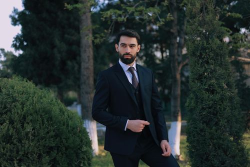 Free A sophisticated man in a suit posing confidently in a lush outdoor garden. Stock Photo