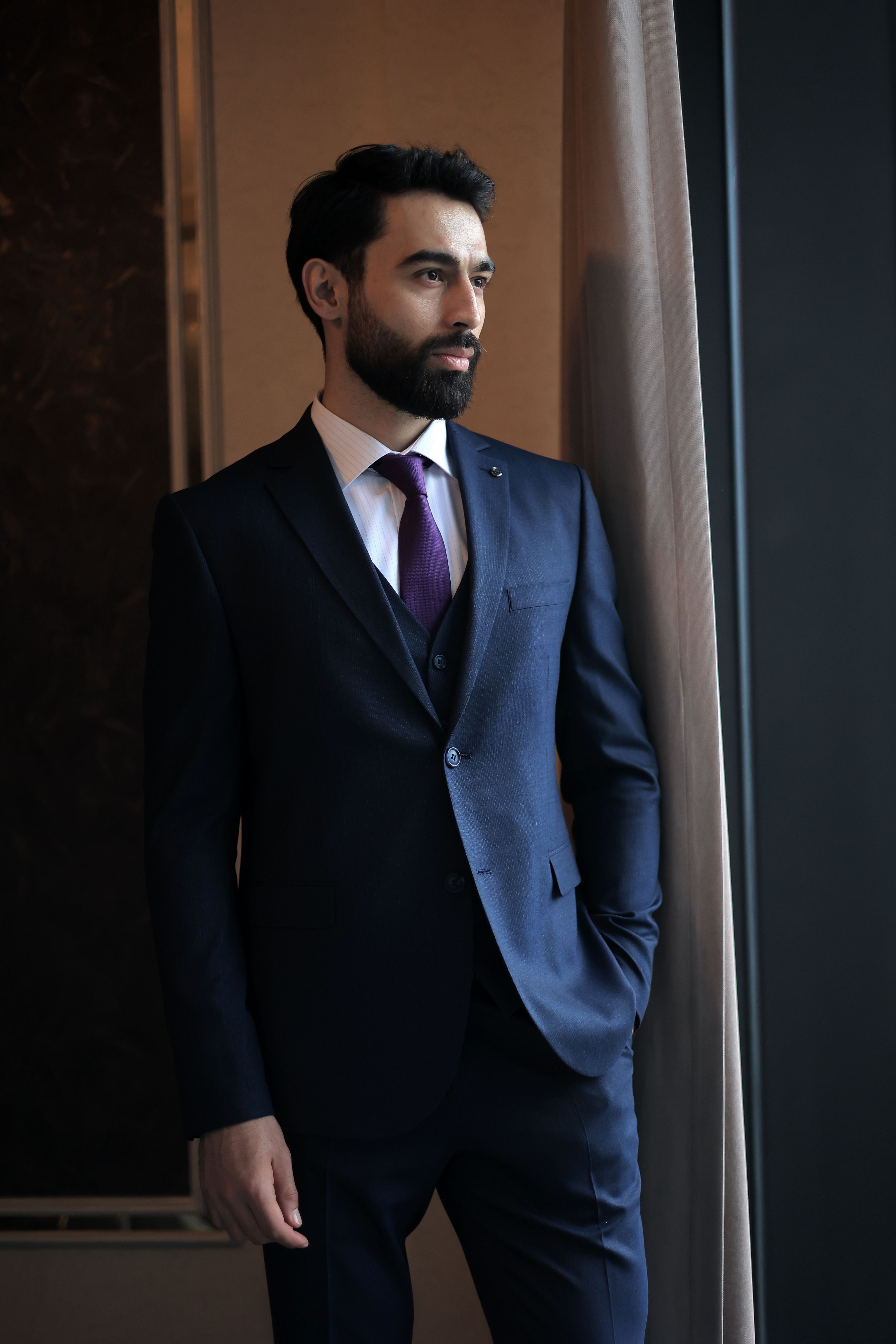 A confident businessman in a navy suit gazing thoughtfully out the window. - Accessories that Complement Men's Dresses