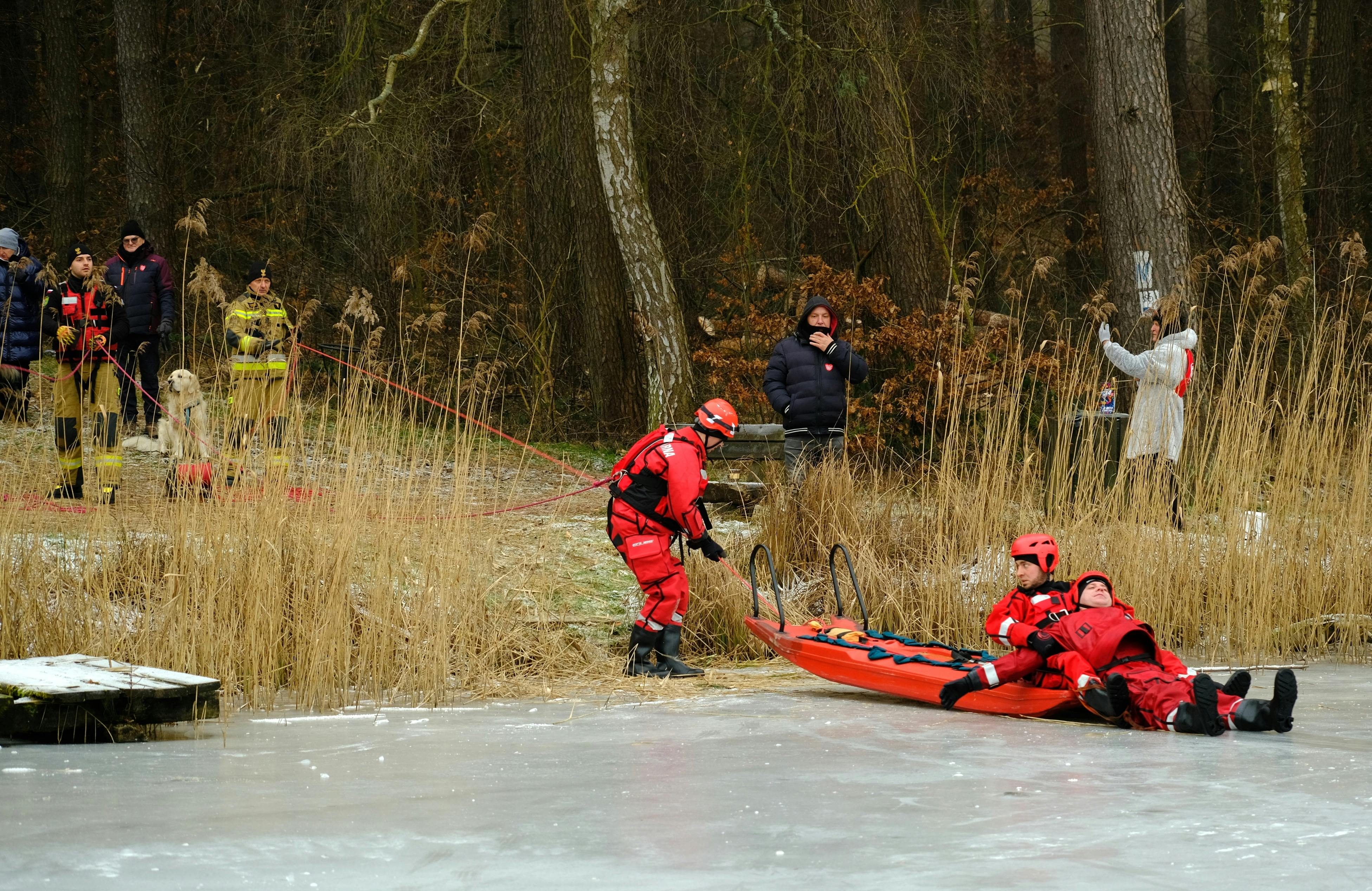 Rescue team practices ice rescue techniques on frozen lake in forest.