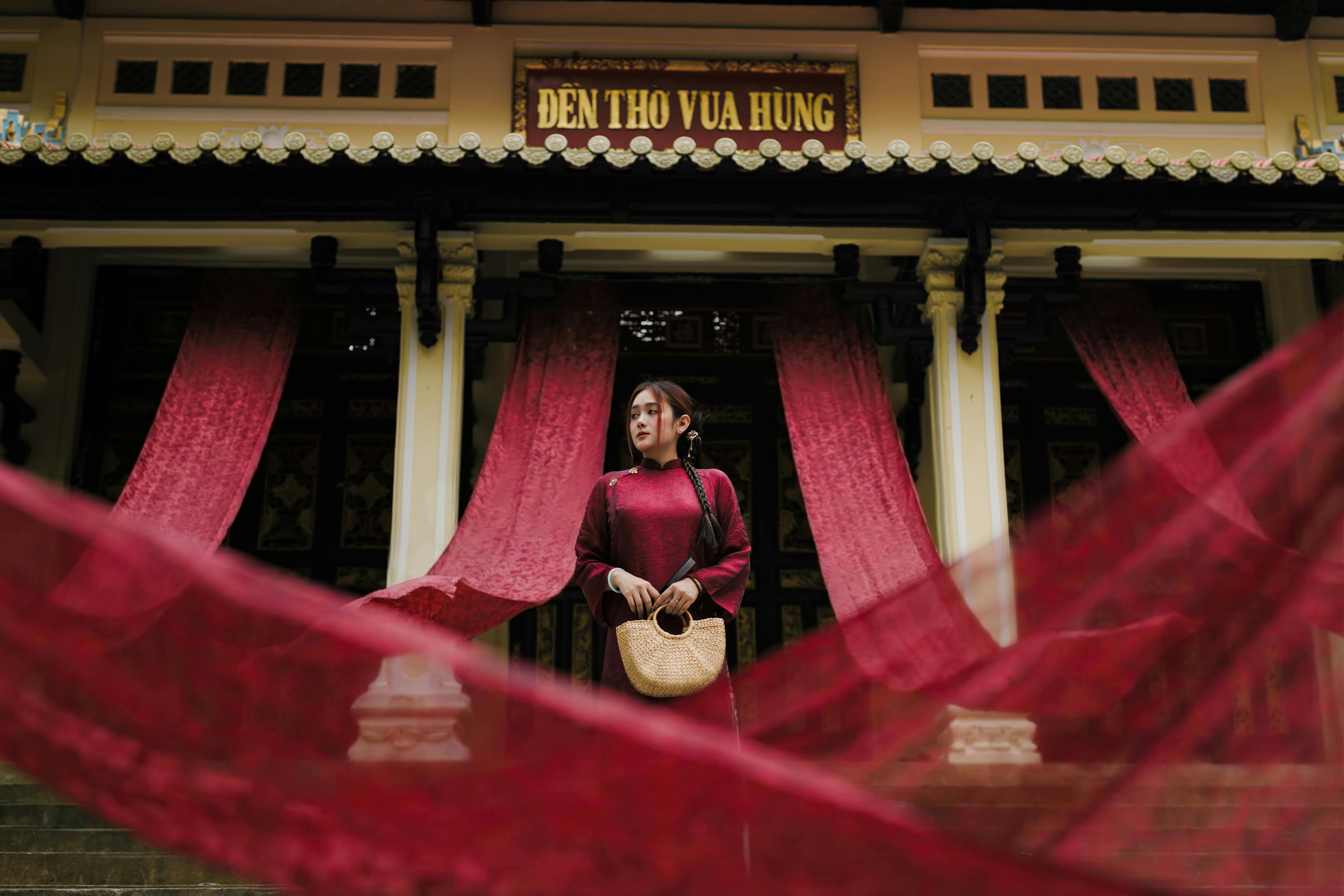 A woman wearing a red traditional dress stands at Den Tho Vua Hung temple, surrounded by red drapes.