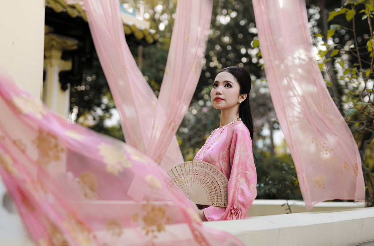 a woman in traditional pink attire holds a fan amidst flowing fabrics