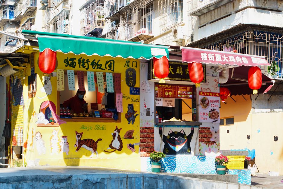 Vibrant cat-themed street food stalls with red lanterns in an urban setting, radiating a lively atmosphere.