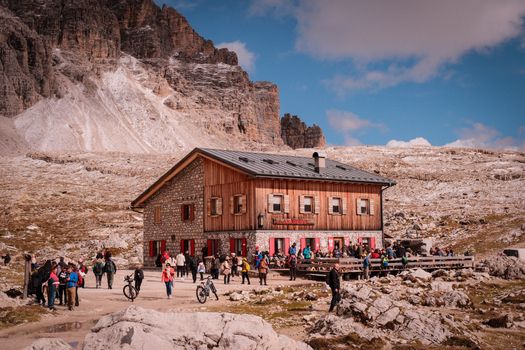 Scenic view of a stone mountain lodge in the Dolomites, surrounded by tourists enjoying the outdoor atmosphere.