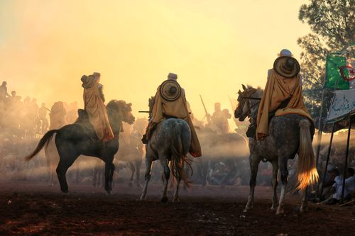 Free Horsemen in traditional attire ride elegantly through a hazy setting at sunset, showcasing cultural heritage. Stock Photo