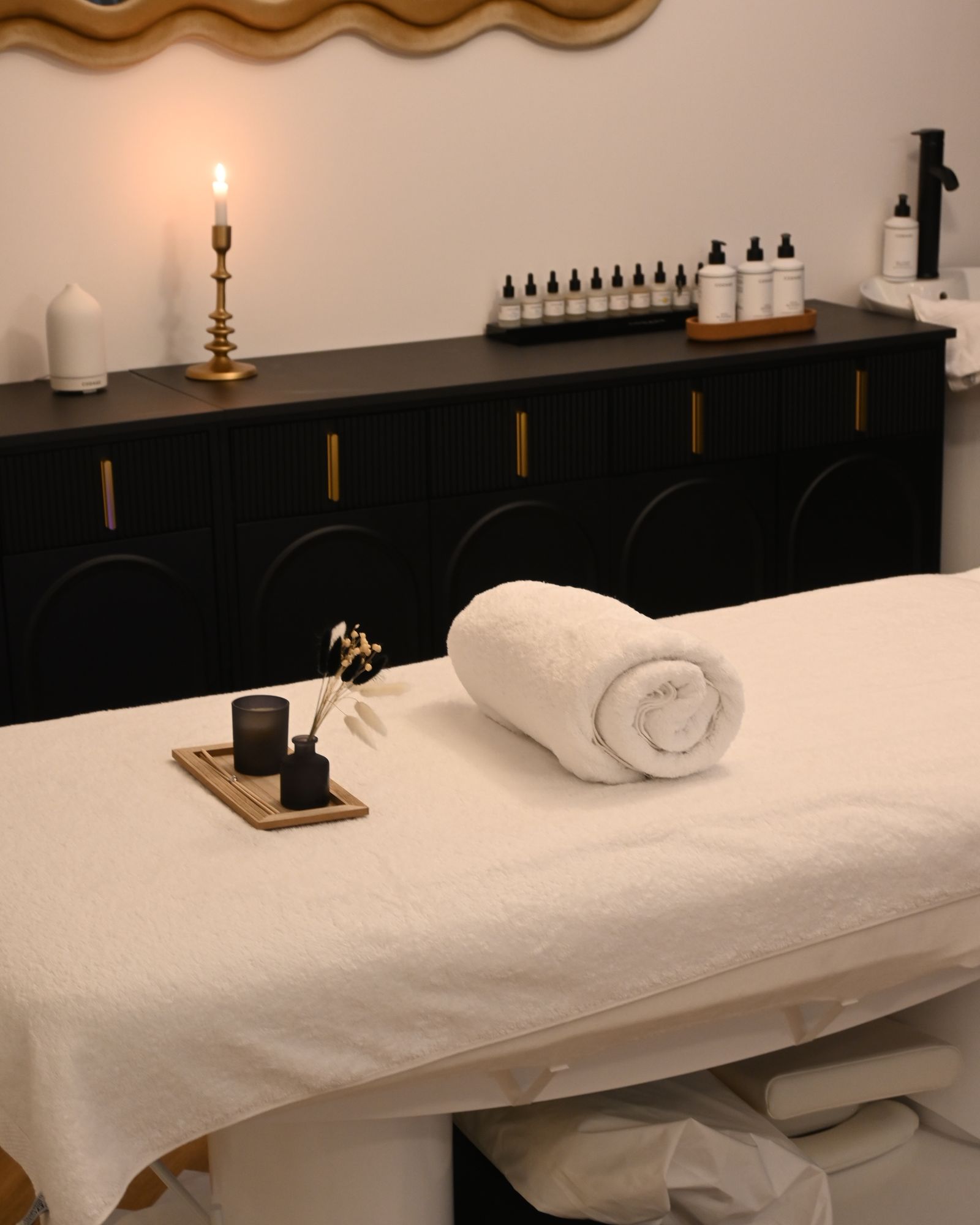 Treatment bed beside a black dresser with oils and a lit candle