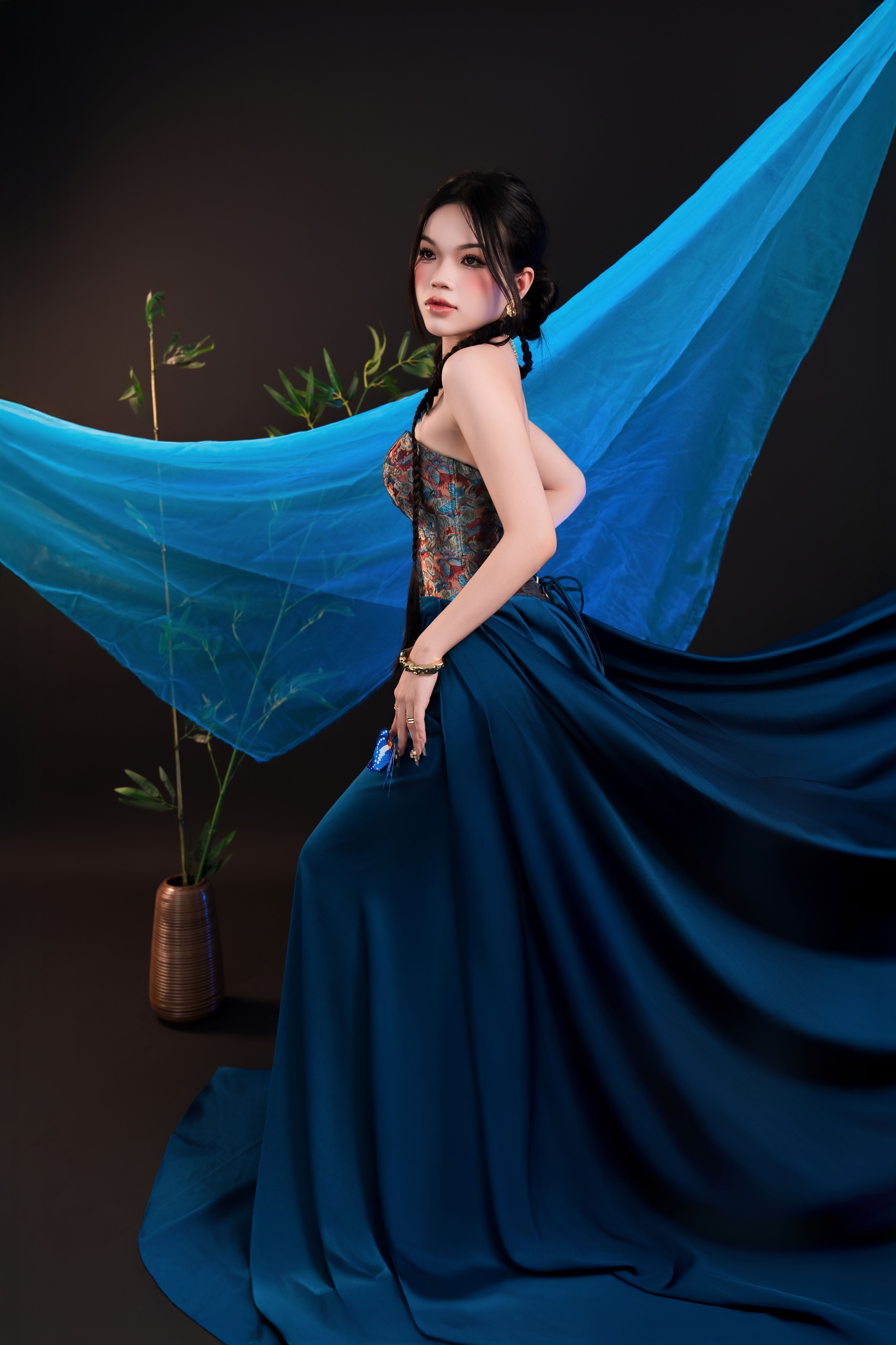 A woman poses elegantly in a blue dress against a striking artistic backdrop indoors.