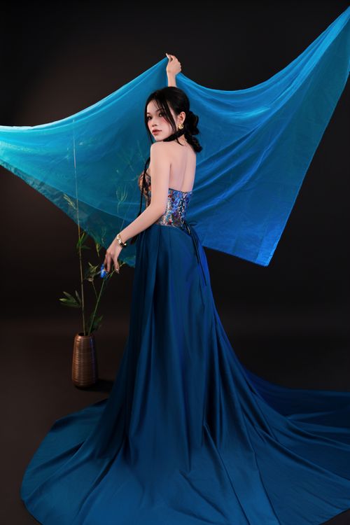 Free Graceful woman poses in a flowing blue gown with delicate fabric drapes, creating an elegant and artistic look. Stock Photo