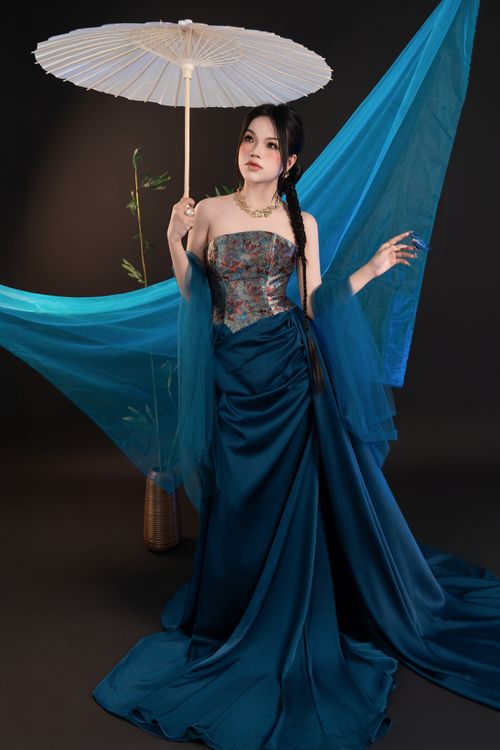 Free A woman in a traditional gown holding a parasol with a graceful pose, set against a vibrant backdrop. Stock Photo