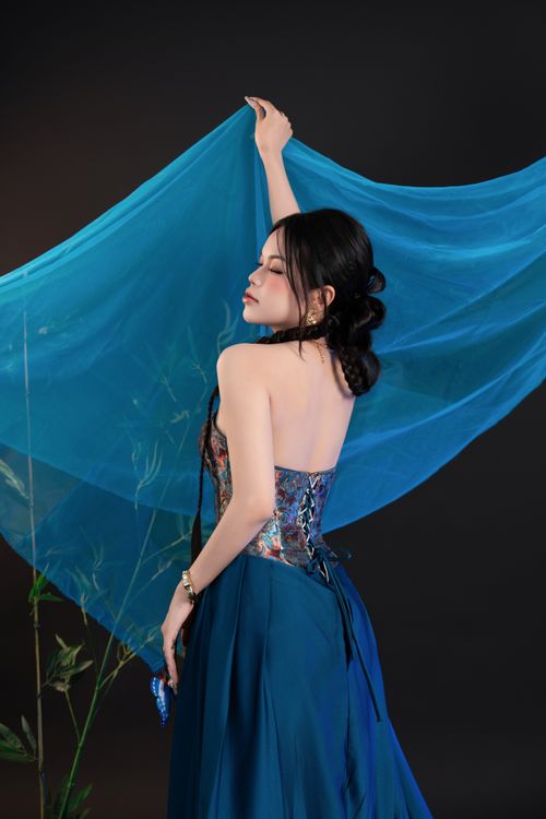 Free Graceful woman in elegant dress posing with flowing blue fabric against a dark studio background. Stock Photo