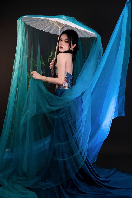 Free Artistic portrait of an elegant woman posing with a white umbrella draped in flowing blue fabric. Stock Photo