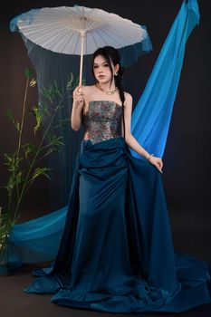 Stylish photo of a woman in an elegant dress holding an umbrella with a blue decorative background.