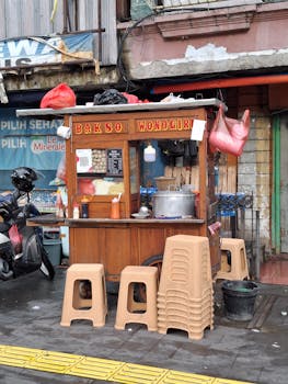 A traditional Bakso street food cart with stacked chairs and cooking utensils in a bustling urban area.