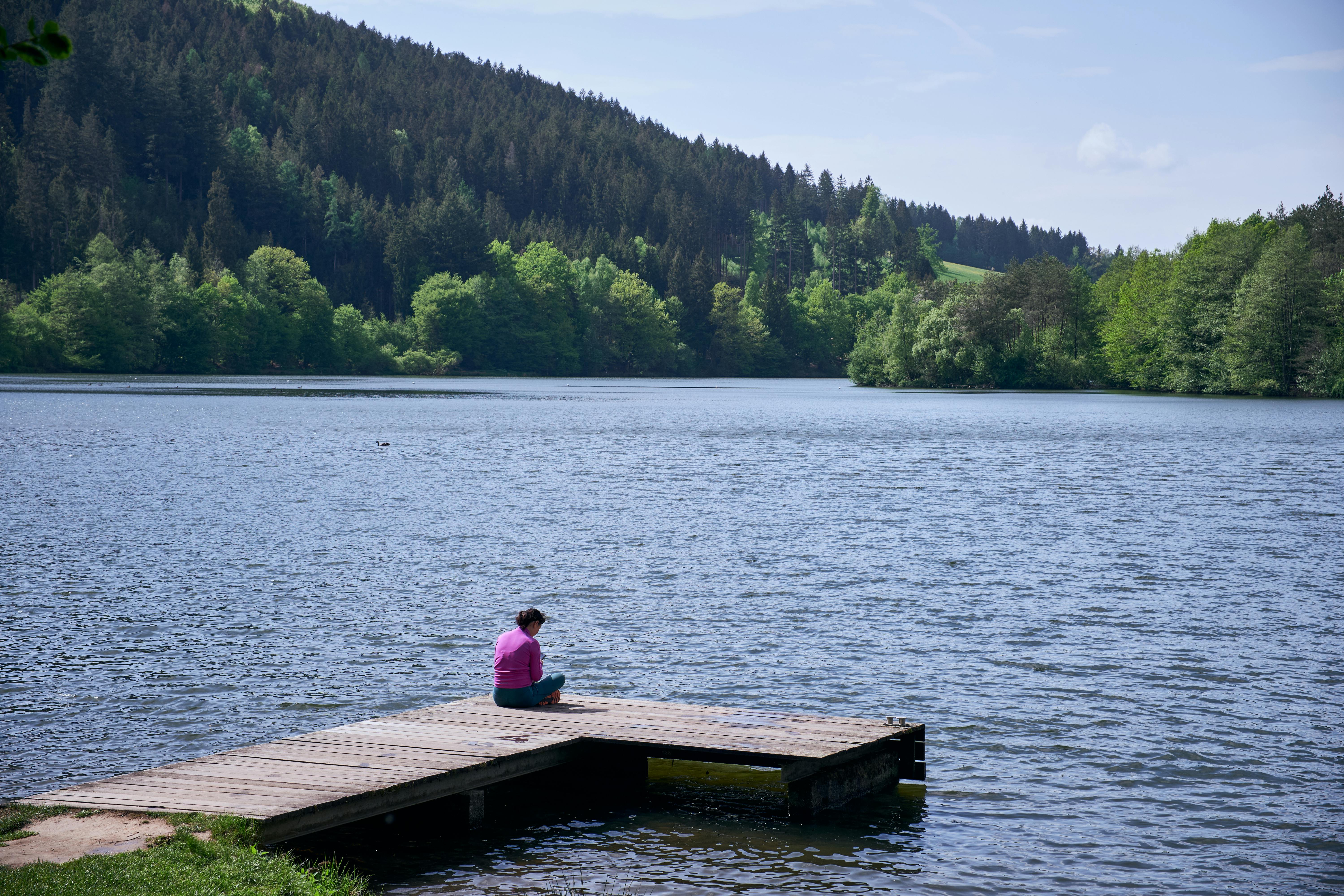 A woman meditates on a wooden dock overlooking a serene forest lake in Hessen, Germany.