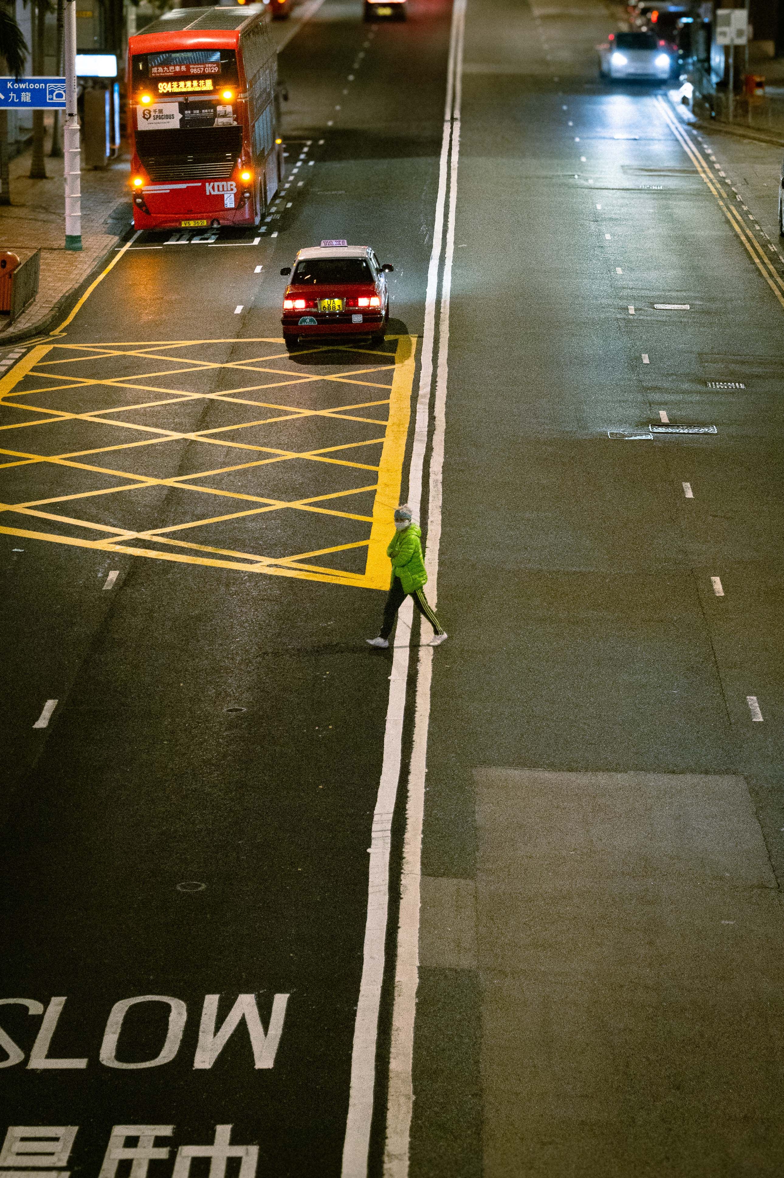 A lone pedestrian crossing a city street at night with vibrant lights.