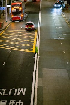 A lone pedestrian crossing a city street at night with vibrant lights.