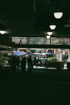 Shadowy view of an urban underpass leading to a lively street market on a sunny day.