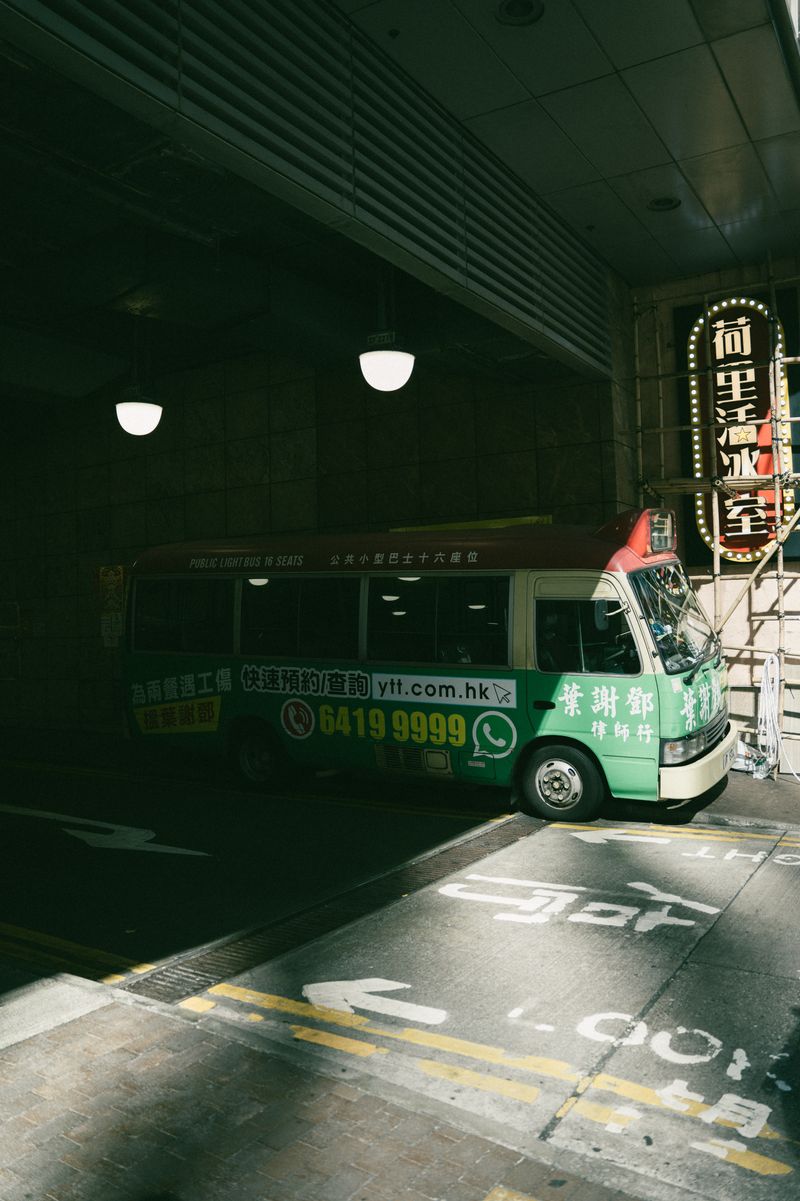 A green minibus in a dimly lit urban tunnel, featuring neon signage and dramatic shadows.