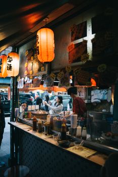 Bustling Japanese street food market with lanterns and diverse people enjoying local cuisine.