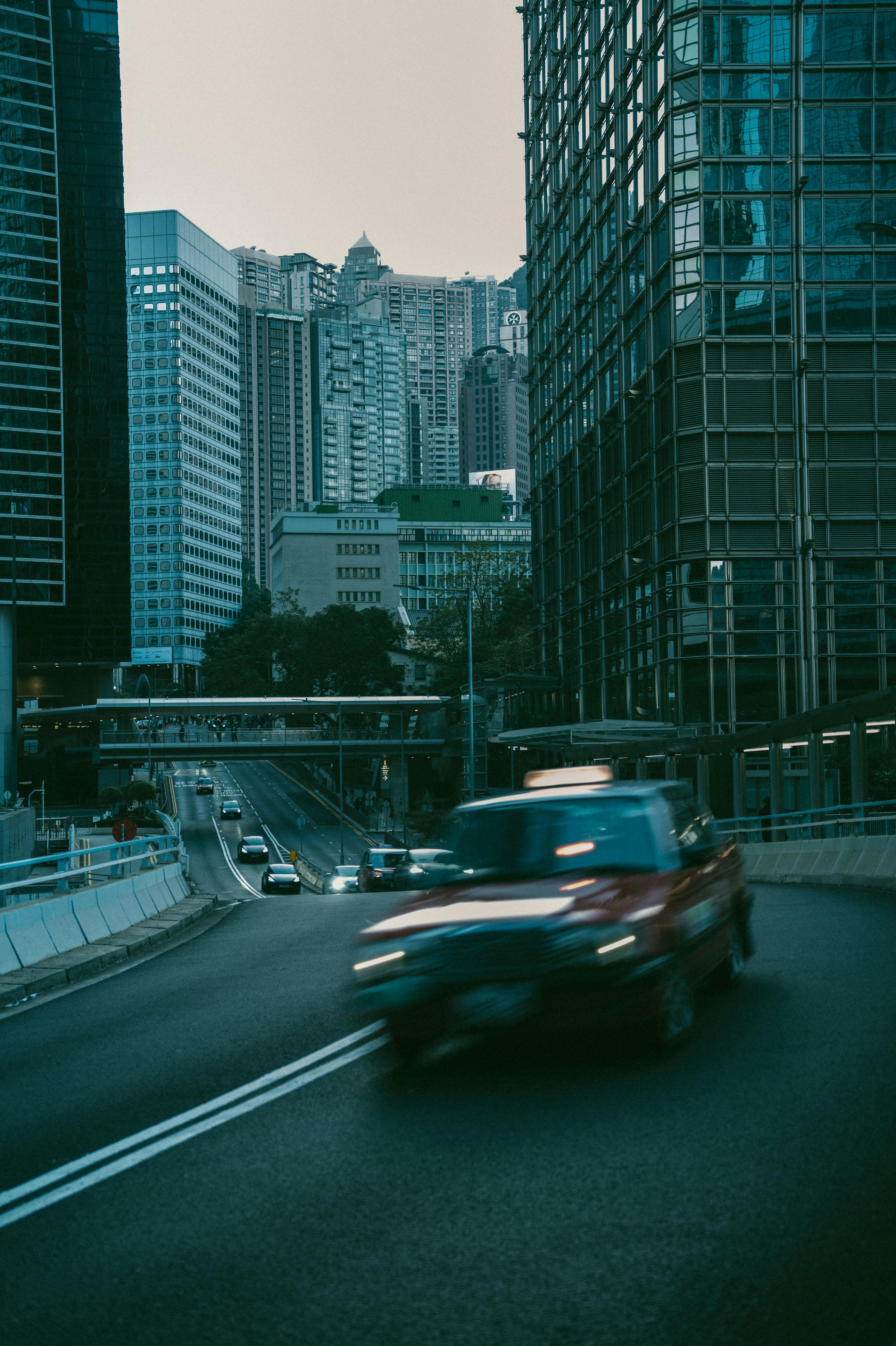 bezplatná Rozmazané červené auto na rušné městské ulici obklopené mrakodrapy za soumraku. Základová fotografie