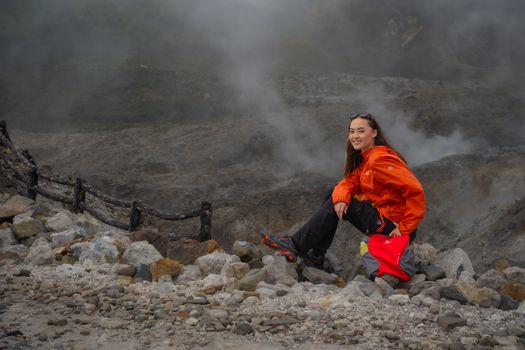 Woman in orange jacket enjoying volcanic landscape at Tangkuban Parahu, West Java, Indonesia.