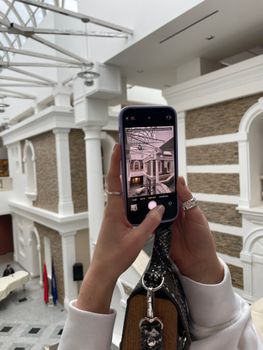 Hands holding phone taking photo of elegant indoor building interior with architectural details.