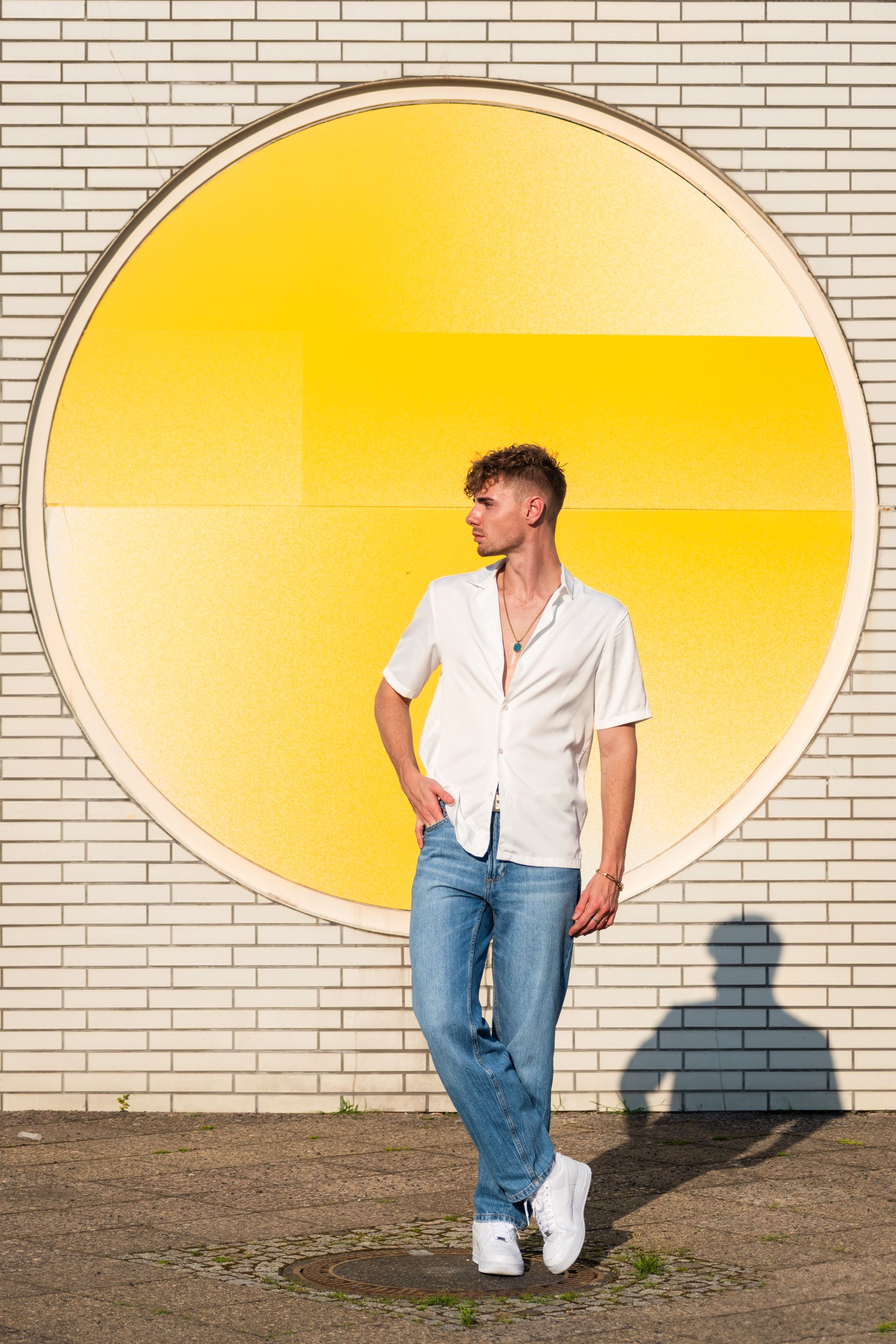 Man in casual attire posing against a vibrant yellow circular wall.