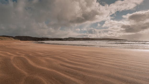 Peaceful beach with striking cloud formations and distant hills, perfect for nature enthusiasts.
