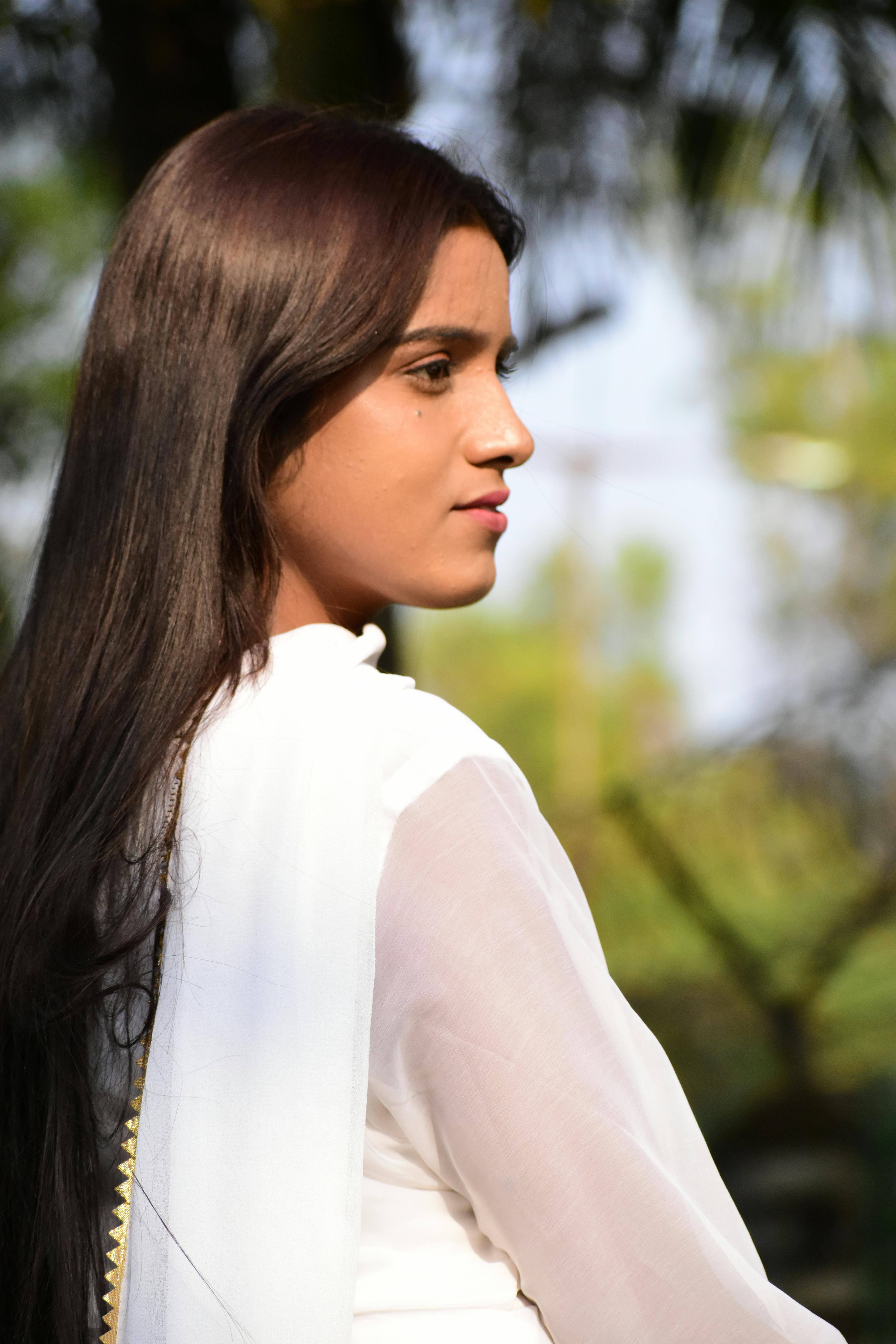 Side profile of a young woman with long hair in a white outfit, captured outdoors.