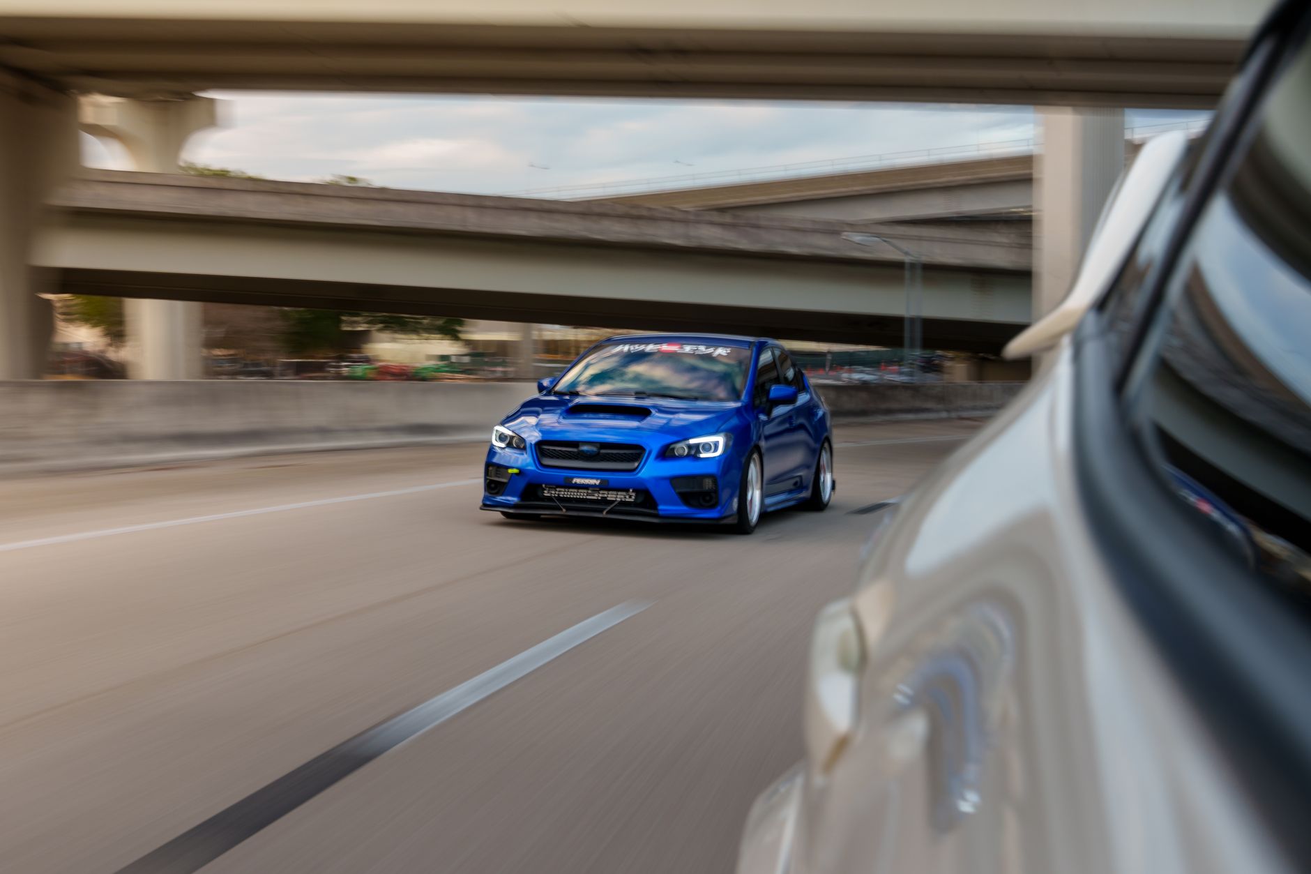 Dynamic shot of a blue sports car racing down a city highway under overpasses.