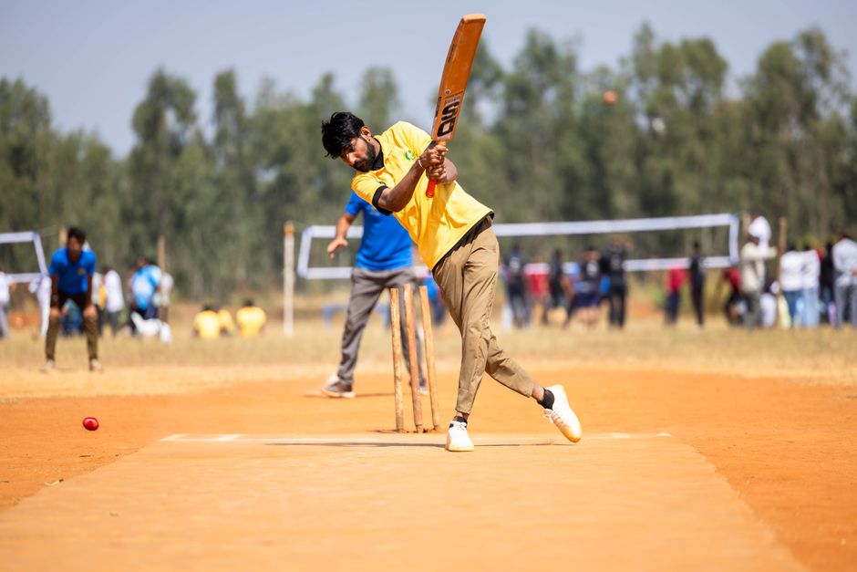 A cricketer in yellow shirt hitting a shot during an outdoor match on a sunny day.