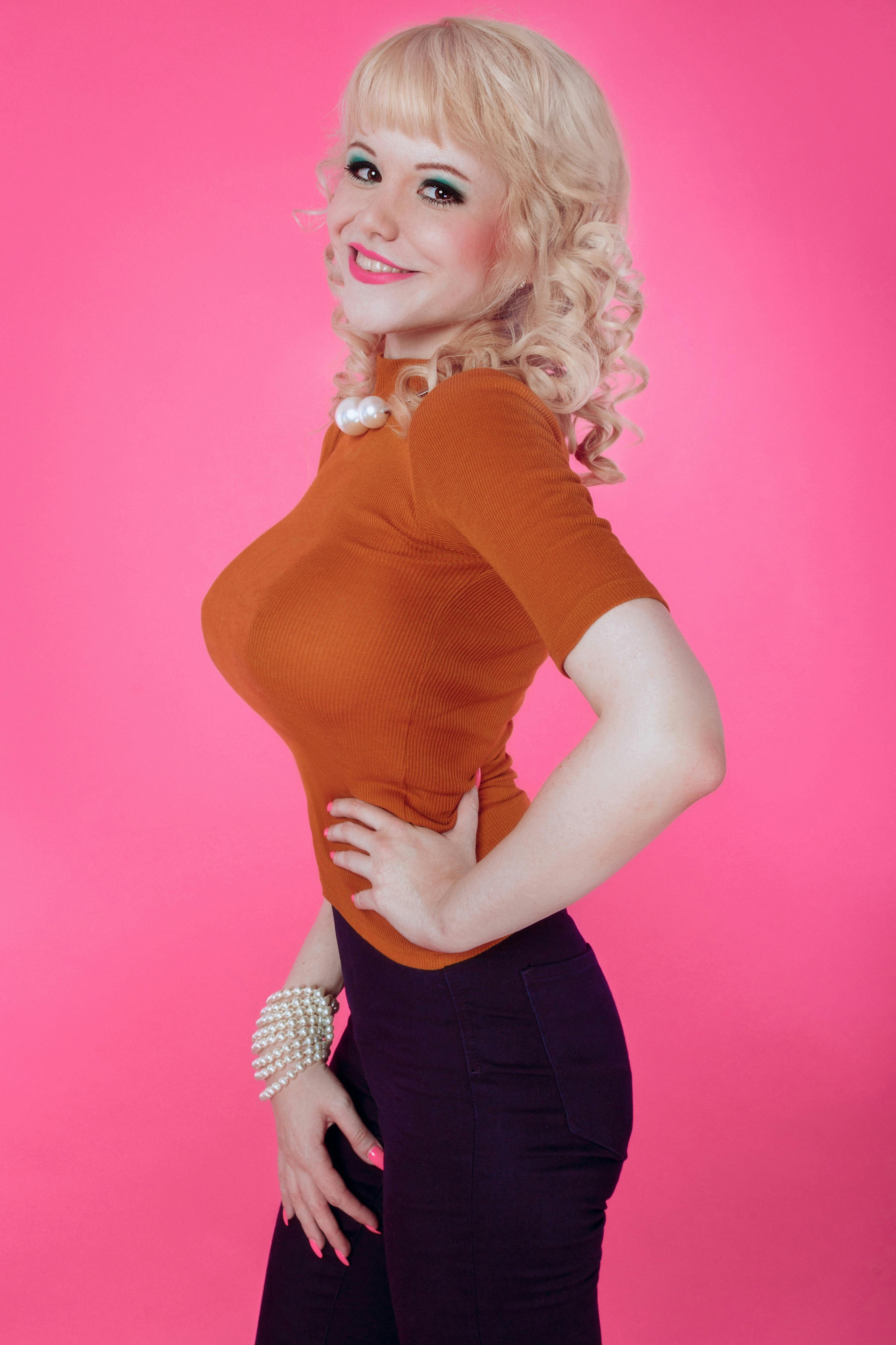 Kostenlos Elegante blonde Frau in orangefarbenem Oberteil posiert selbstbewusst vor einem leuchtend pinkfarbenen Hintergrund. Stock-Foto