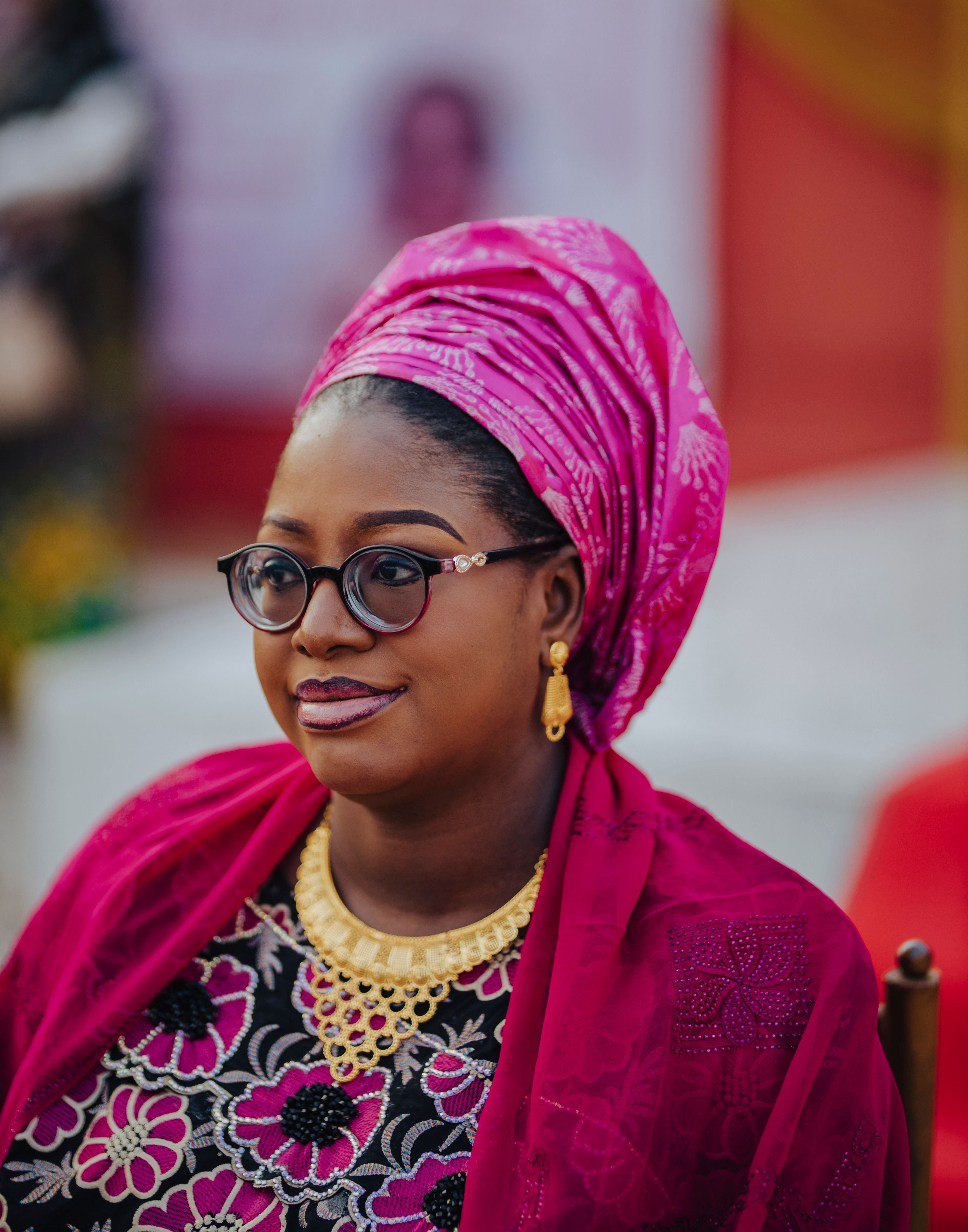 Woman adorned in vibrant pink headscarf and traditional jewelry, indoors.