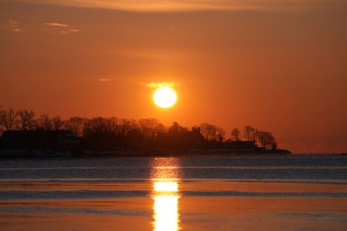 Free Breathtaking sunset over a calm lake with silhouetted trees reflecting in water. Stock Photo