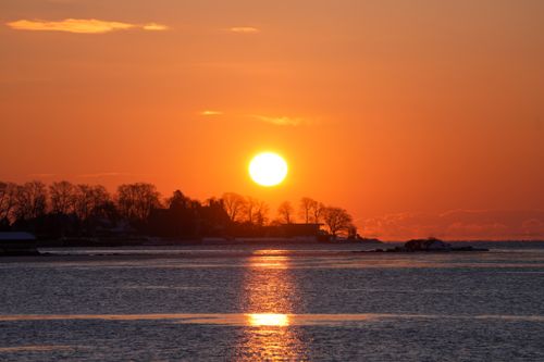 Free A breathtaking sunset over a serene ocean with silhouetted trees and buildings. Stock Photo