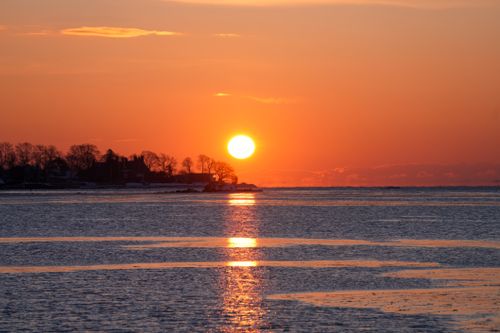 Free Serene coastal sunset with orange hues reflecting over calm ocean waters. Stock Photo
