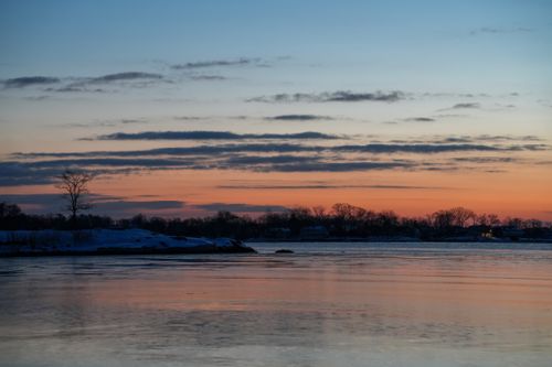 Free Tranquil winter sunset reflecting on a frozen lake with silhouetted trees. Stock Photo
