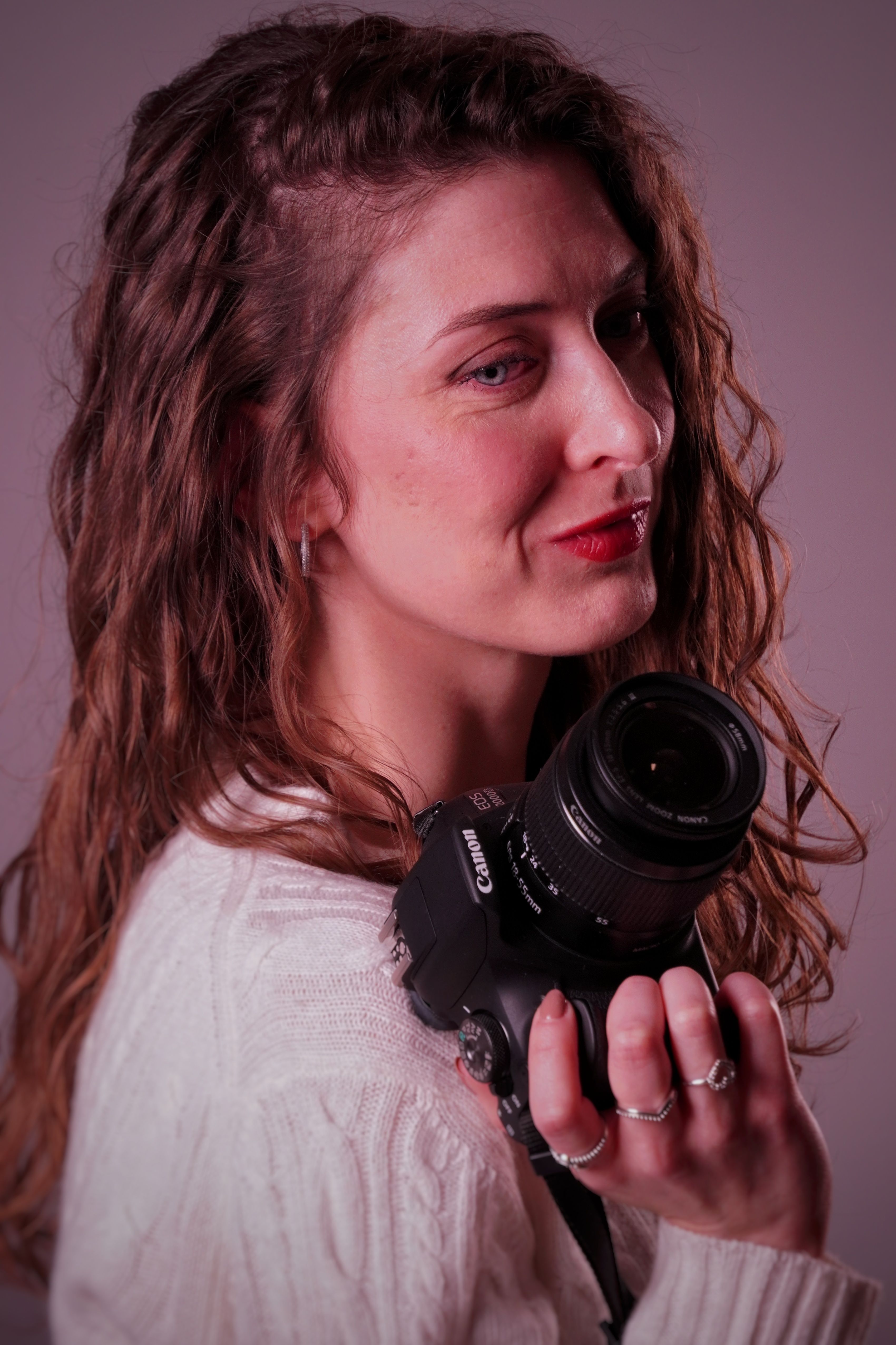 Smiling young woman with curly hair holding a camera, ready for photography.