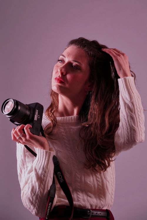 Free Young woman photographer holding a camera in a studio setting, captured in a thoughtful pose. Stock Photo