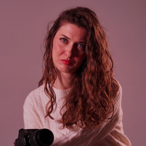 Free Portrait of a young woman holding a camera against a plain background, exuding creativity and focus. Stock Photo