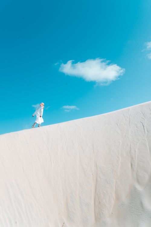 Free A person in white attire walking across sand dunes in Mambrui, Kenya. Stock Photo