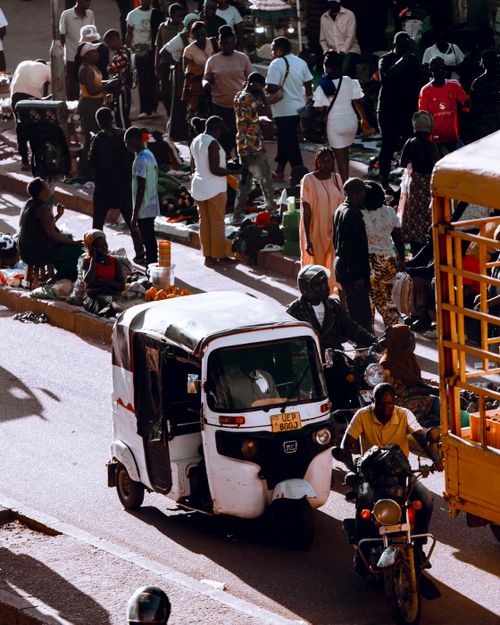 Free Bustling street market in Kampala, Uganda, showcasing local vendors, pedestrians, and a tuk tuk on a sunny day. Stock Photo