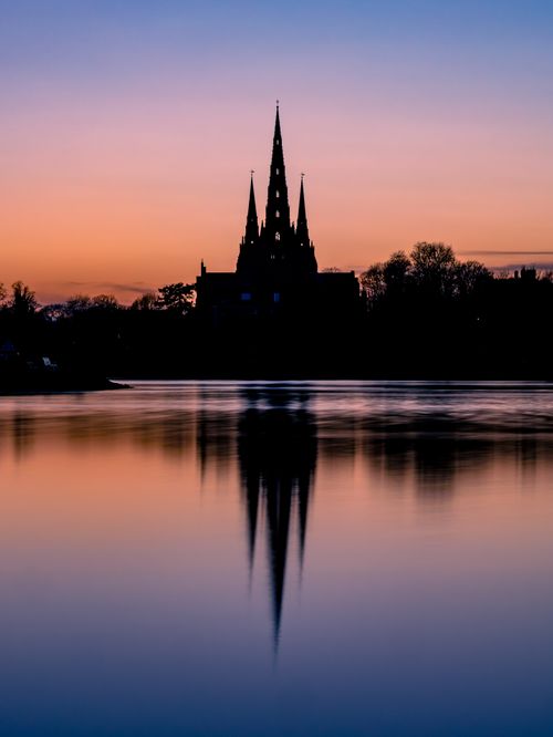 Free Capture of Lichfield Cathedral silhouette reflecting on Stowe Pool during sunset in England. Stock Photo