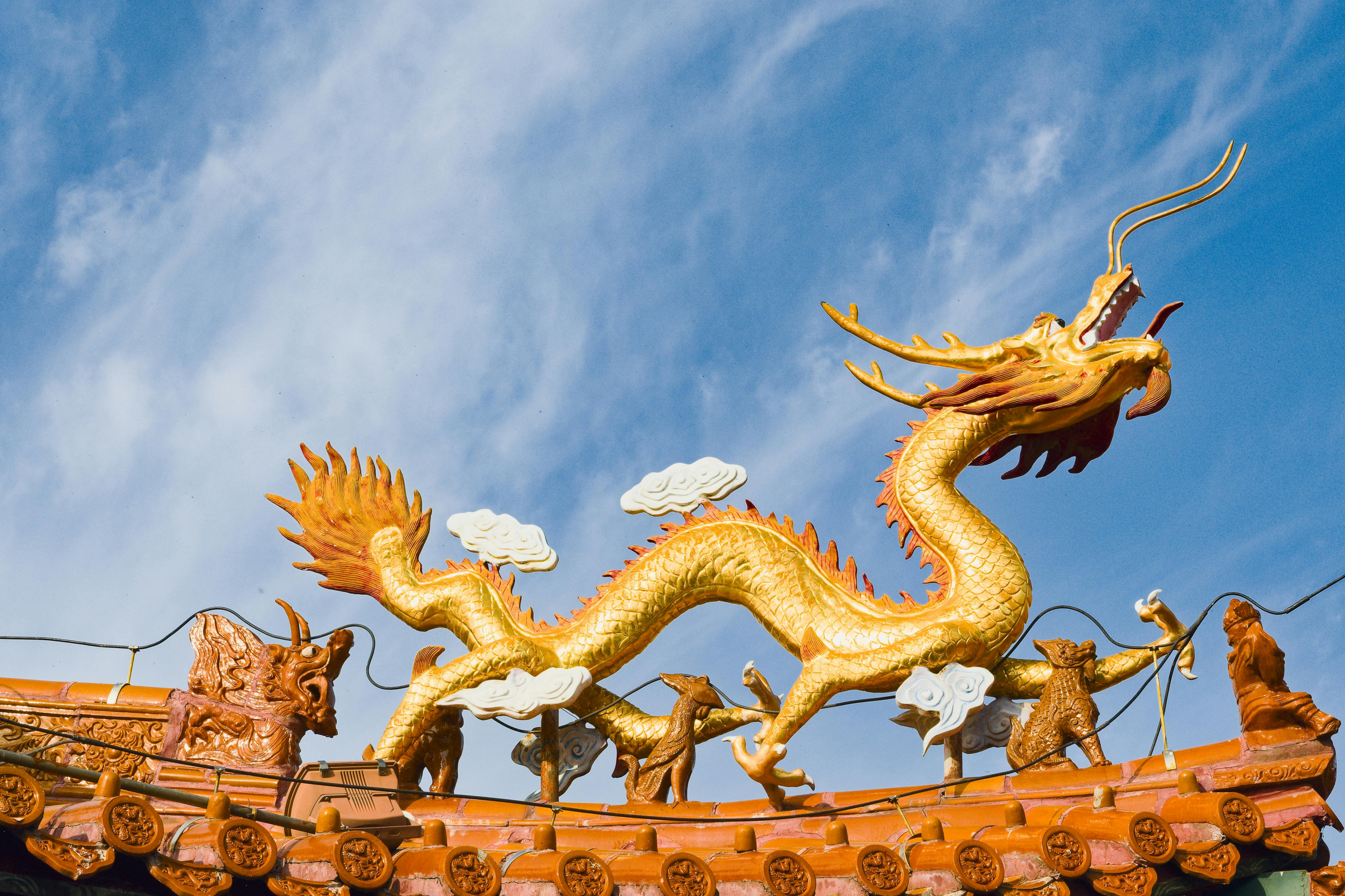 Magnificent golden dragon sculpture on a traditional Chinese temple roof under a clear blue sky.