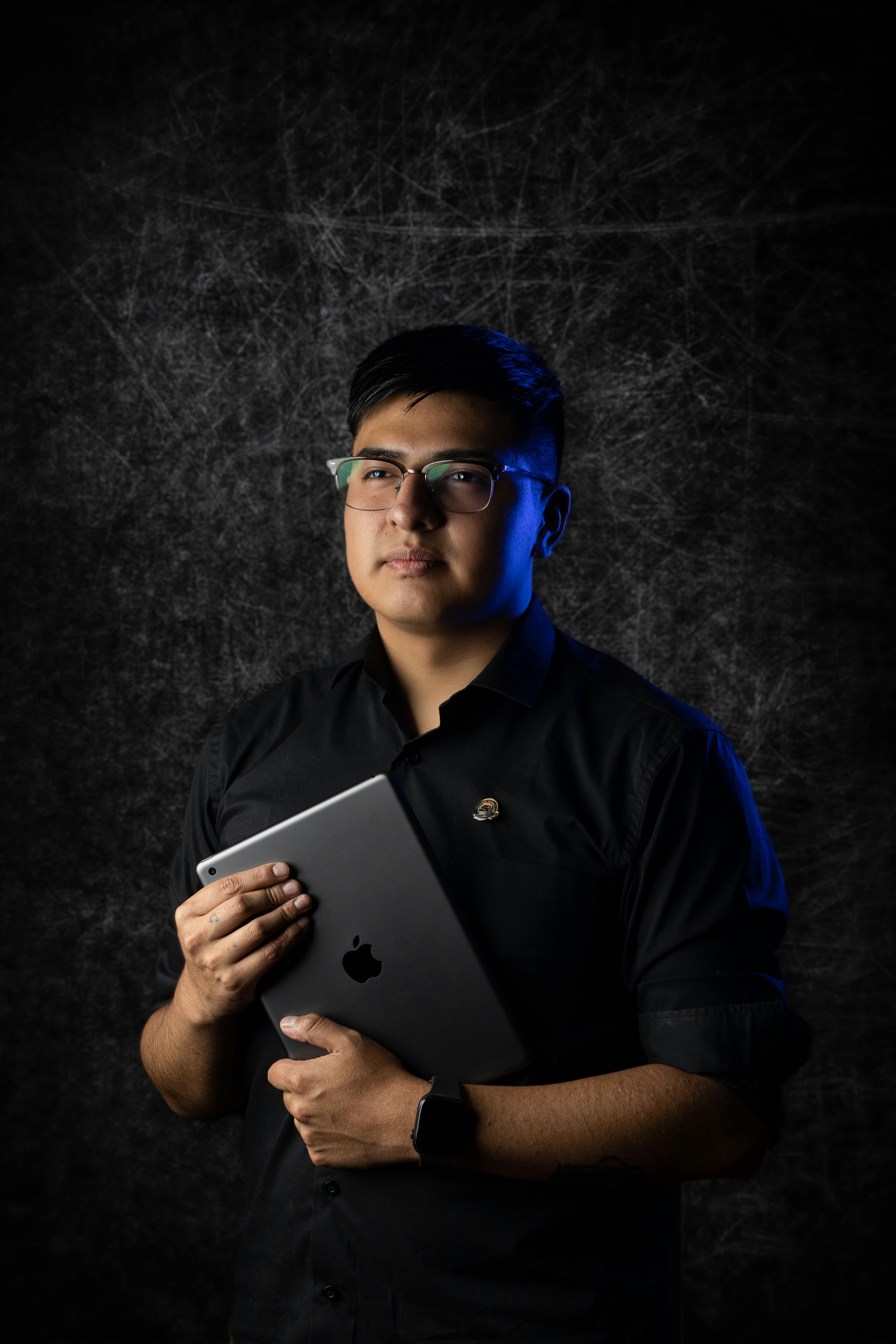 бесплатная На этом атмосферном студийном портрете молодой человек держит в руках изящный планшет, демонстрируя современные технологии. Стоковое фото