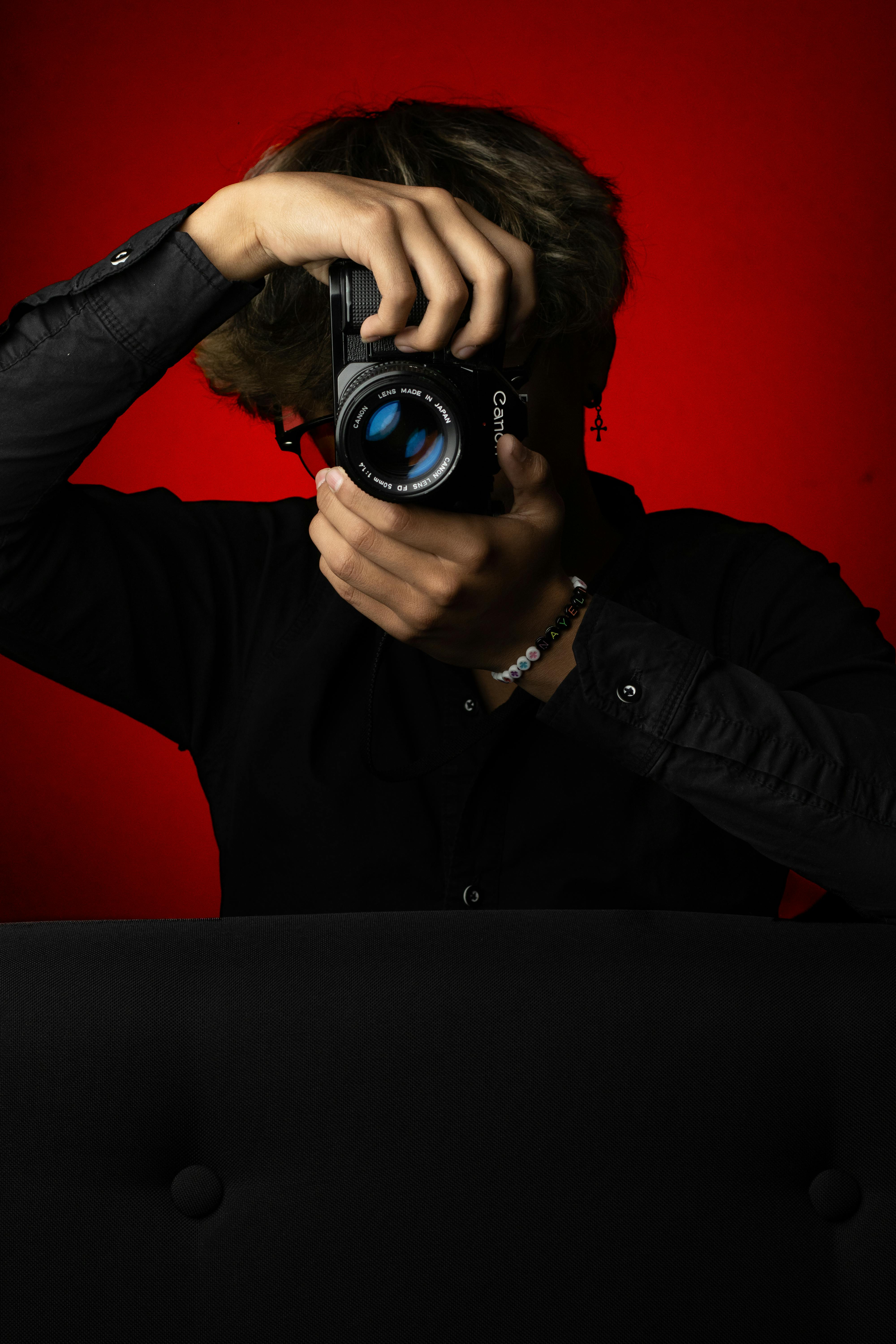 grátis Pessoa segurando uma câmera contra um fundo vermelho vibrante, criando arte dramática. Foto profissional