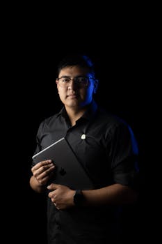 Professional studio portrait of a man holding a tablet against a black background.