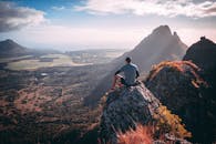 一名徒步旅行者坐在山顶，欣赏着山谷的优美风景和远处山峰的壮丽景色