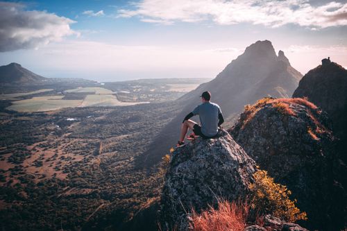 Free A hiker sits on a mountaintop, taking in a breathtaking view of a scenic valley and distant peaks. Stock Photo
