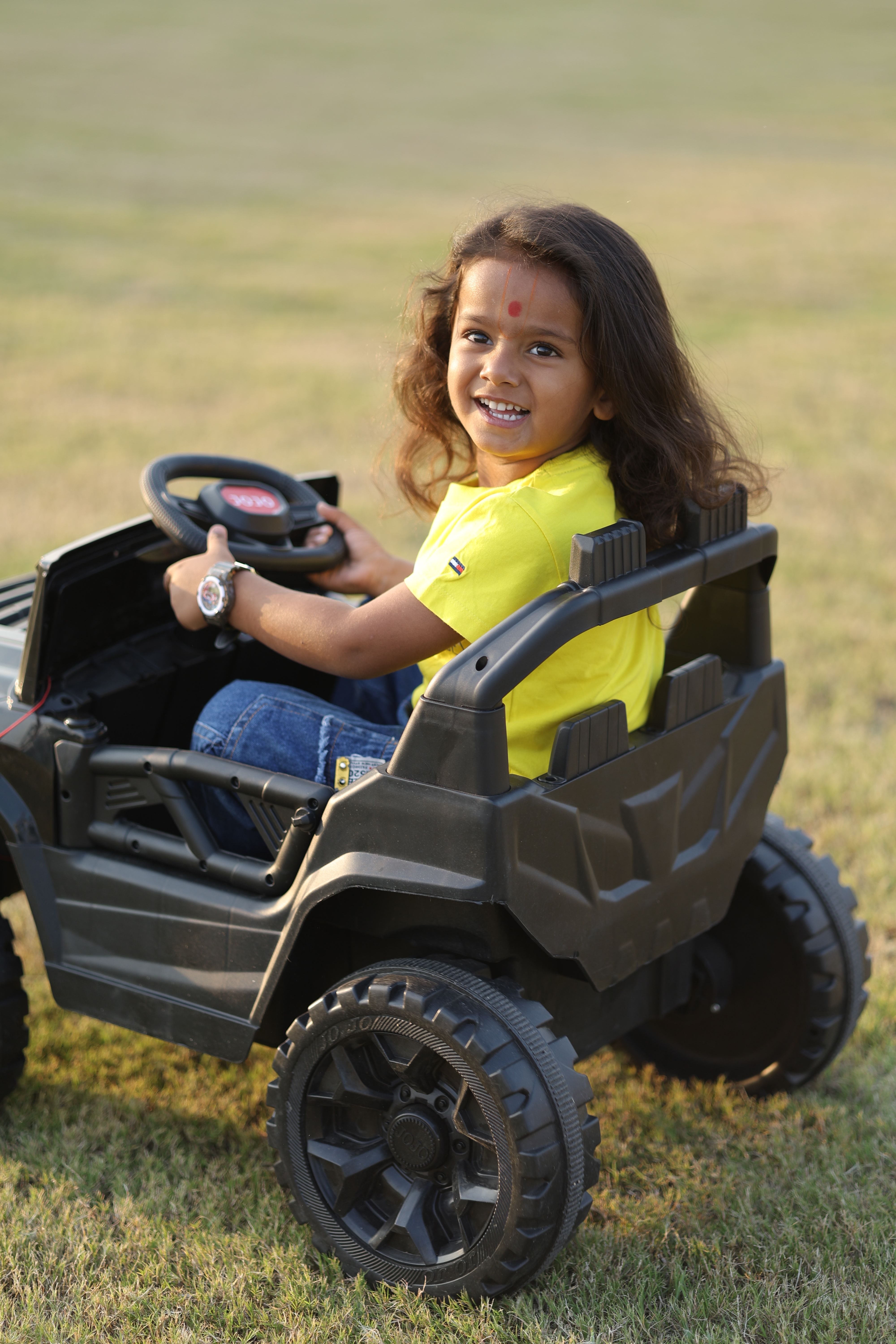 A cheerful child enjoys riding a toy car on a sunny day in the park.